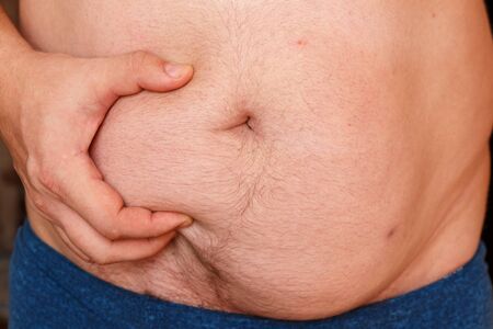 A man holds his stomach with his hand and shows his fat.の写真素材