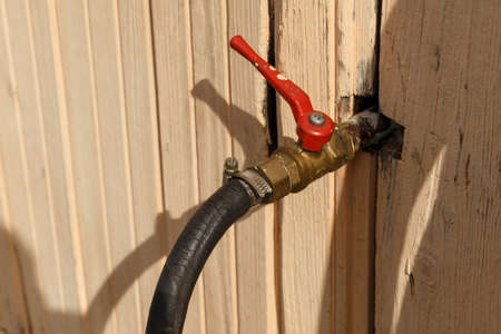 The water tap is sticking out of the wall of the house. Iron water tap with a red handle.の写真素材
