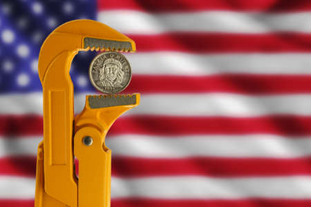 three Cuban peso coin held in an orange plumber wrench against the background of the usa flagの写真素材