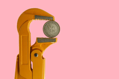 One hundred shillings Uganda coin held in an orange plumber wrench on a pink backgroundの写真素材