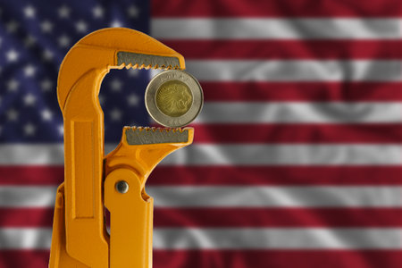 Ethiopian one Birr coin held in an orange plumber wrench on the background of the flag of the United States. Obverse of the coin.の写真素材
