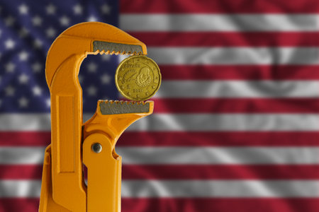 20 euro cent coin held in an orange plumber wrench on the background of the flag of the United States. Obverse of the coin.の写真素材
