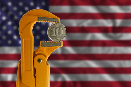 Kyrgyzstani ten som coin clamped in an orange plumber wrench on the background of the flag of the United States. reverse sideの写真素材
