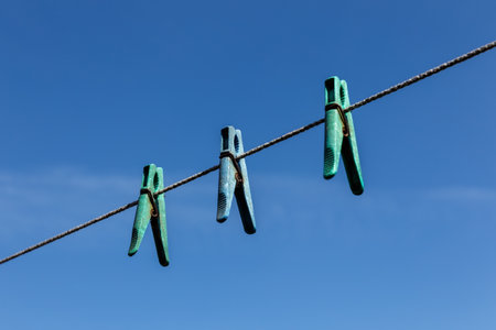 Three plastic clothespins hanging on a clothesline against a blue sky.の写真素材