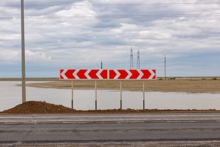 Red arrow signs warn drivers of a sharp curve ahead on a road adjacent to a flooded area under a...