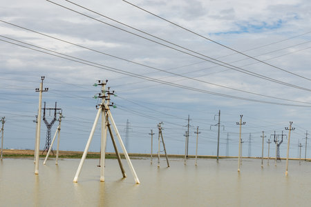 Power lines stand tall above rising waters, showcasing a rural landscape affected by recent flooding. The sky is overcast with cloudsの写真素材