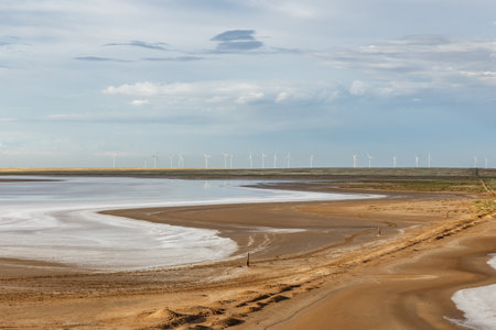 A calm salt lake stretches across the horizon, dotted with wind turbines under a vast sky in Kazakhstan's landscape.の写真素材