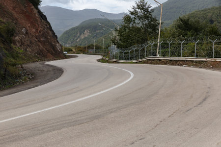 A winding road runs along the border of Iran and Azerbaijan, surrounded by mountains and greenery on...
