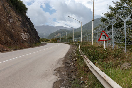A winding road follows the terrain near the Iran-Azerbaijan border, surrounded by mountains and security fencing reflecting a tense atmosphere.の写真素材