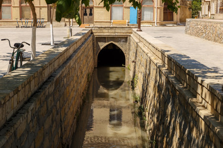 Visitors take in the serene water channel featuring traditional stone architecture in Bukhara, Uzbekistan, showcasing the city's rich history.の写真素材