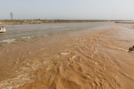 The Vakhsh river meanders through Kyzylkala, showing strong currents and brown waters under a clear sky, highlighting the region's natural beauty.の写真素材