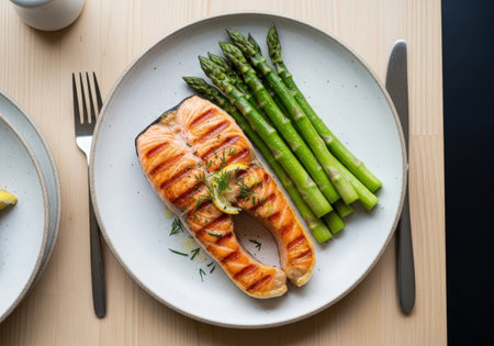 A top view of a healthy grilled salmon steak. Served on a rustic plate with fresh green asparagus, a slice of lemon, and a dill garnish for dinner.の素材