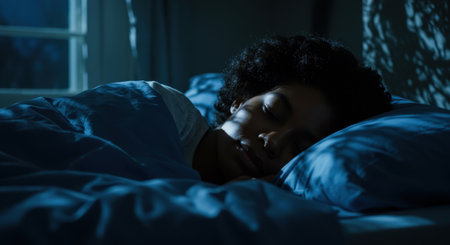 Young woman deep in tranquil slumber, peacefully resting in bed at night. Cool ambient light softly illuminates her face, casting gentle patterns across the quiet room.の素材