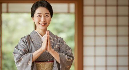 Beautiful middle-aged Asian woman in a traditional gray kimono dress, smiling and greeting in a Japanese room with shoji screens in the background.の素材