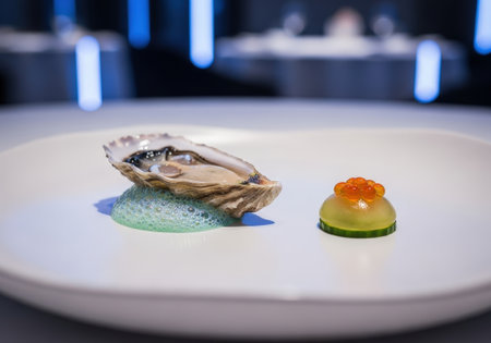 An elegant gourmet appetizer of a single fresh oyster. Served on a white plate with foam, cucumber, and red caviar in a luxury restaurant setting.の素材
