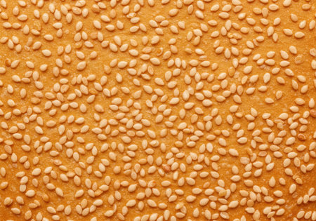 Small, light-colored sesame seeds cover a warm golden background, showing their natural texture and color. Ideal for culinary uses.の素材