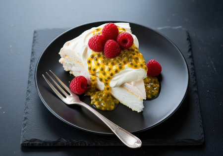A delicious slice of pavlova meringue cake. This dessert features a crisp crust and is topped with whipped cream, fresh raspberries, and passion fruit.の素材