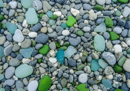 Colorful sea glass and smooth pebbles with bubbles underwater on a beach. A natural treasure background from a top down view.の素材