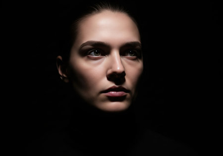 Dramatic close up beauty portrait of a woman's face emerging from the dark. An artistic chiaroscuro style shot with high contrast.の素材