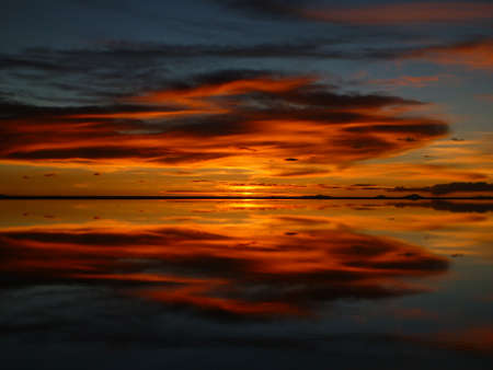 A red sunset that reflects like a mirror on the surface of the water at Uyuni salt lake in Boliviaの写真素材