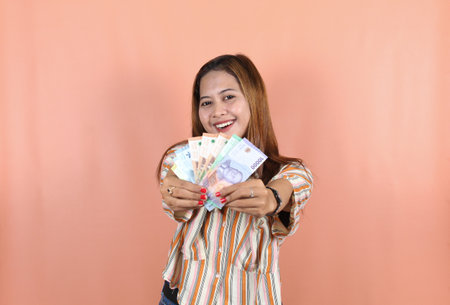 A happy young woman is wearing striped dress with brown hair and holding cash money in Indonesian...
