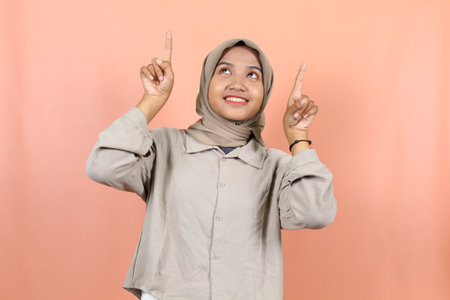 Excited Asian woman wearing purple sweeter pointing at the copy space beside her, isolated by peachÂ backgroundの写真素材