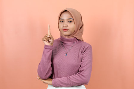 Happy young  muslim asian woman pointing to empty place in purple sweater isolated over peach backgroundの写真素材