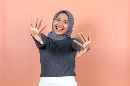 beautiful young asian woman greeting with open palms wearing a purple sweater isolated peachÂ backgroundの写真素材