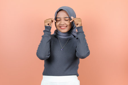 beautiful young Asian woman in love pose with fingers using both hands near face with eyes closed while smiling showing teethの写真素材