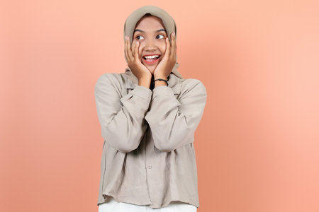 A beautiful young Asian woman is holding her cheeks with both hands while looking up and smiling while showing her teethの写真素材