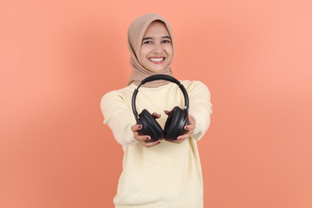 happy beautiful young Asian muslim woman showing headphone.  advertising and greeting wear earphone...