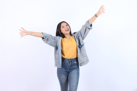 Excited young Asian female wearing blue jacket yellow t-shirt with raised hands open five fingers celebrating success, enjoy life isolated on whiteの写真素材