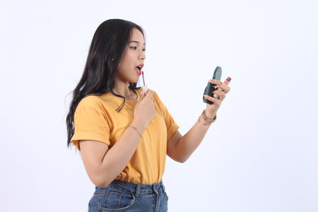 Beautiful young Asian woman using lipstick with a small miror in her hand, makeup fashion beauty isolated white backgroundの写真素材