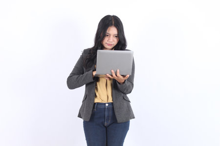 Woman is holding a laptop and looking at it. She is wearing a gray suit and blue jeans.の写真素材