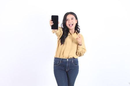 Beautiful girl expressive showing blank screen on phone. She is wearing a yellow shirt and blue jeans. Business asian womanの写真素材