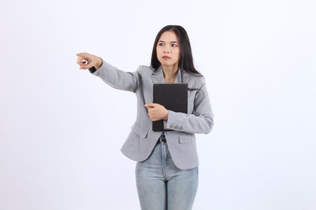 Woman in a gray blazer points to asides with hugging a book in her hand. She looks serious and focused. Business asian womanの写真素材