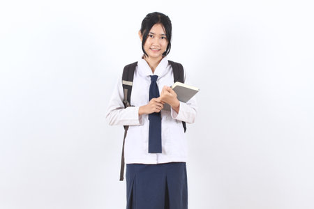 A girl wearing a school uniform and bag holding a book. She is smiling. Concept of happiness and positivityの写真素材