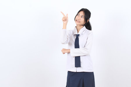 Asian teenage girl with long hair wearing school uniform pointing finger to empty spaceの写真素材