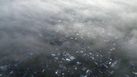 Ethereal drone shot looking down on a town shrouded in thick mist. A mysterious and quiet landscape representing pollution, weather, or climate.の写真素材