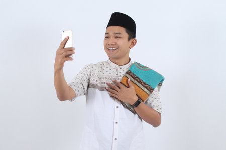 Cheerful Asian Muslim man in traditional clothes makes a video call to greet family for Eid al-Fitr...