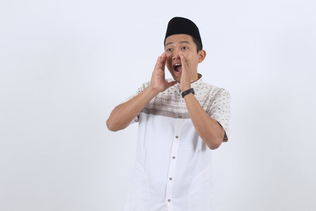 Young Indonesian man in traditional Islamic attire yelling a message. Concept for Ramadan sale, Eid promotion, breaking news, or communication.の写真素材