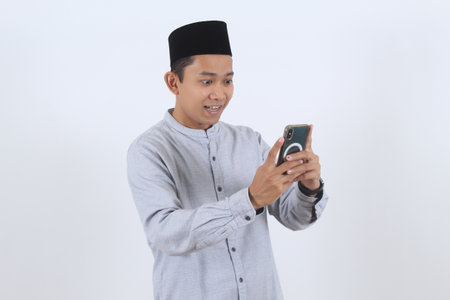 An amazed Indonesian man in Muslim attire reacts to good news on his mobile phone. Great for...