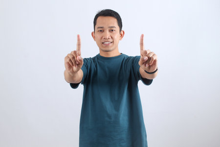 A friendly young Asian man smiles at the camera, pointing up with both index fingers. A positive gesture for success, goals, and making a point.の写真素材