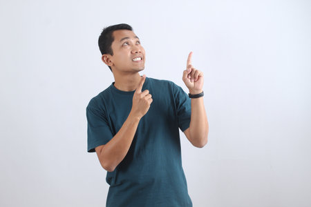 Happy young Asian man looking and pointing up, having a creative idea or solution. Isolated on a plain background with copy space for text.の写真素材