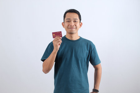 Confident young Asian man smiling, presenting his bank card. E-commerce, cashless payment, easy transaction, and financial satisfaction concept.の写真素材