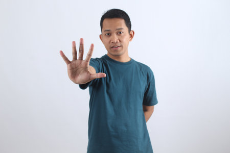Serious young Asian man showing open palm as a warning or stop sign. Concept of denial, rejection, setting boundaries, or saying no. Isolated portrait.の写真素材