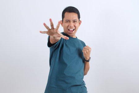 Expressive Asian man yells with a hand reaching out in a stop or grab gesture. Concept of power,...
