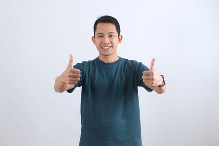 A cheerful and satisfied Asian man smiles while giving two thumbs up, expressing positive feedback, success, and agreement on a white background.の写真素材