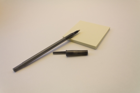 A black pen and its cap with a pad of yellow sticky notes against a white backgroundの写真素材