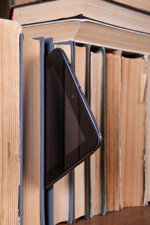 Tablet stands on a bookshelf with old booksの写真素材